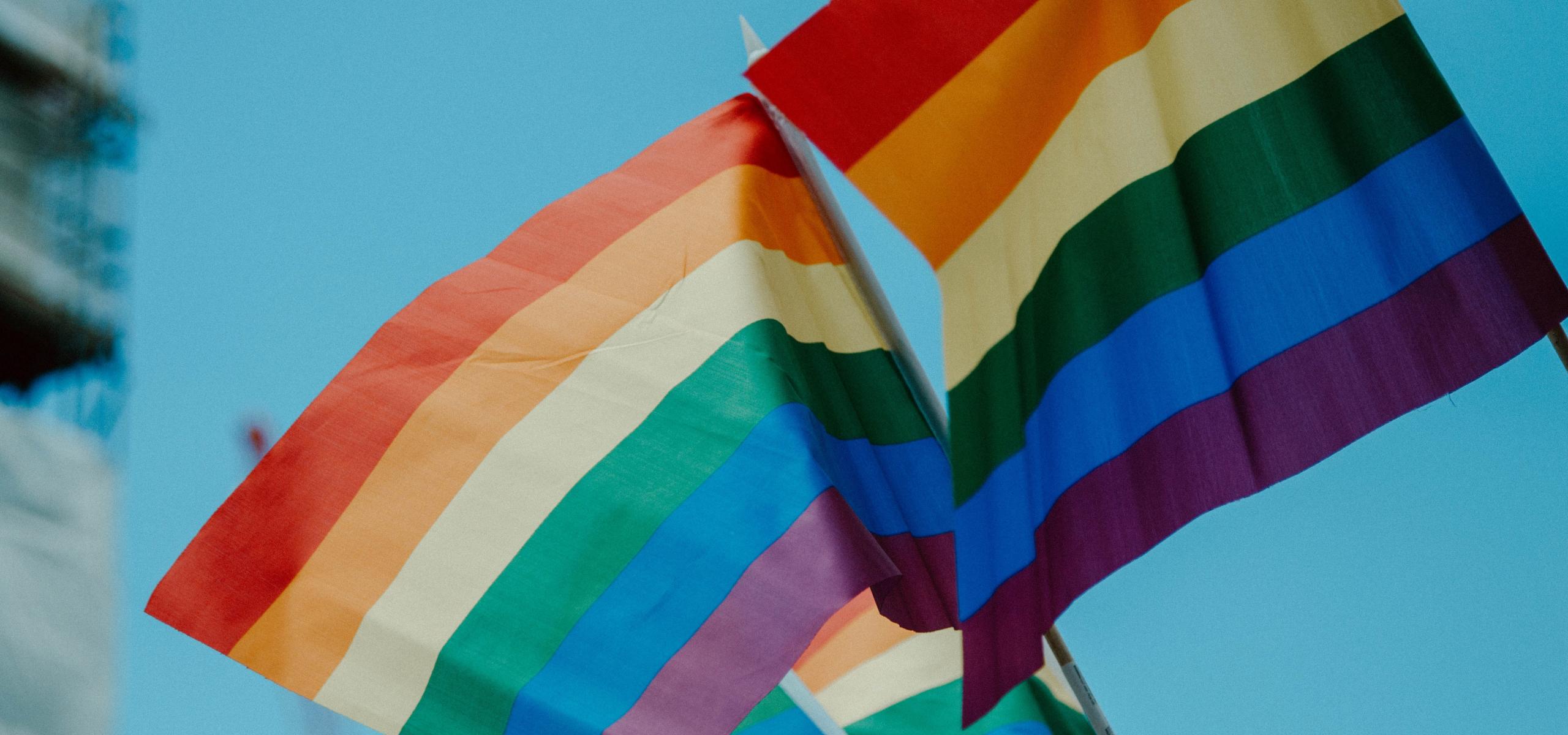Pride flags in the wind, on a blue sky backdrop.